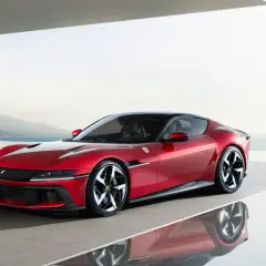 Roter Ferrari mit 12 Zylindern, elegant auf einer reflektierenden Fläche vor einer Küstenlandschaft.