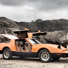 Orange Bricklin SV1 mit Flügeltüren steht auf Schotter vor einer Kiesgrube.