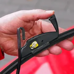 Hand wechselt Scheibenwischer vorne am Toyota Yaris. Der Wischerarm wird mit dem Haken eingehängt.