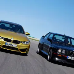 Goldener BMW M4 F80 und schwarzer BMW E30 M3 auf Rennstrecke.