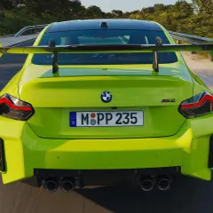 Leuchtend grüner BMW M2 Competition mit großem Heckspoiler rast auf einer Landstraße.