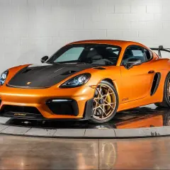 Orange Porsche GT4 RS mit Carbon-Motorhaube und goldenen Felgen, bereit für die Rennstrecke.