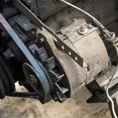Ein alter Keilriemen quietscht an einer Lichtmaschine. Staub und Öl bedecken die mechanischen Teile.