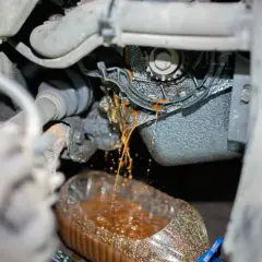 Flüssigkeit tropft aus dem Motorraum in eine Flasche. So merkt man das die Wasserpumpe defekt ist: Rostbraunes Kühlmittel tritt aus.