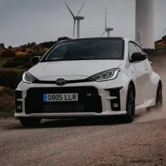 Weißer Toyota C1201 fährt auf staubiger Straße, Windräder im Hintergrund.