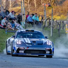 Porsche rast durch das Rebenland bei der Rallye, Zuschauer säumen die Strecke.