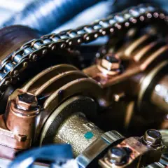 Detailaufnahme einer metallischen Steuerkette eines Autos, die über Zahnräder läuft.
