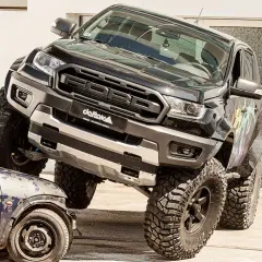 Schwarzer Ford Ranger mit **Ford Duratorq**-Motor überfährt ein kleines Auto. Offroad-Umbau mit riesigen Reifen.
