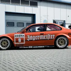 Orange BMW E36 Motorsport-Rennwagen mit Jägermeister-Lackierung und goldfarbenen Felgen.