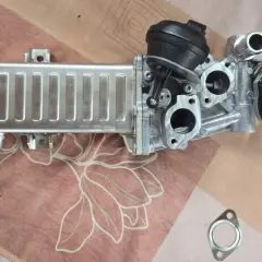 VW AGR-Kühler mit schwarzem Stellmotor und gelber Kappe auf gemustertem Untergrund.