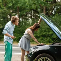Mann zeigt auf Motorhaube, Frau schaut hinein. Sie fragt sich, ob sie mit einem abgassystem defekt weiterfahren kann.