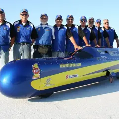 Ein Team steht stolz neben einem stromlinienförmigen Fahrzeug, das aussieht, als wäre es das schnellste Motorrad der Welt.