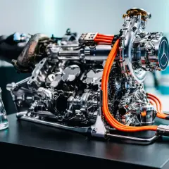 Ein hochmoderner F1 Motor, glänzend und komplex, mit leuchtend orangen Kabeln. Daneben ein Kolben und ein Becherglas mit Flüssigkeit.