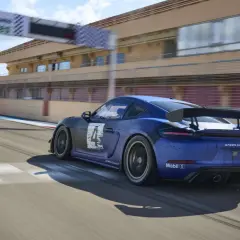 Blauer Porsche 718 Cayman GT4 Clubsport auf Rennstrecke, mit Start-/Zielbogen im Hintergrund.