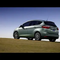Ein hellgrüner Ford C-Max Energi Plug-in Hybrid steht auf einem grasbewachsenen Hügel unter blauem Himmel.