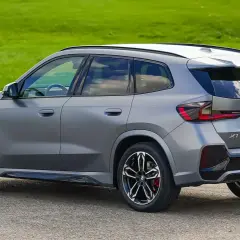 Grauer BMW X1 23d steht auf Asphalt vor grüner Wiese.
