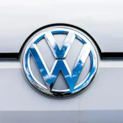 Das glänzende VW-Logo auf dem silbernen Lack reflektiert den blauen Himmel mit Wolken. Ein p0016 vw.