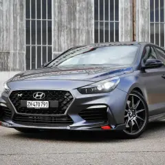 Grauer Hyundai i30 N Project C mit roten Akzenten vor Holzwand.