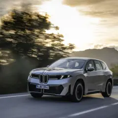 Silberner BMW iX3 fährt auf einer Straße im Sonnenuntergang. Informieren Sie sich über die Lieferzeiten des BMW iX3.