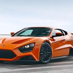 Ein leuchtend oranger Sportwagen, ein Symbol für schnelle Autos, steht auf einer Terrasse mit Blick auf das Meer.