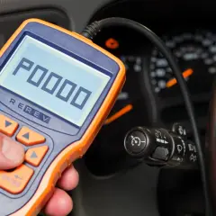 OBD-II-Diagnosegerät zeigt Fehlercode P0000 an. Ein Mann hält das Gerät in der Hand, während im Hintergrund das Armaturenbrett eines Autos zu sehen ist.