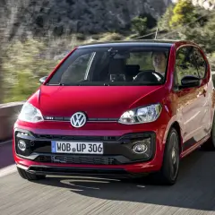 Roter VW Up GTI fährt auf einer kurvigen Straße mit Bäumen im Hintergrund.