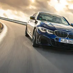 Blauer BMW M340i fährt auf einer kurvigen Straße bei Sonnenuntergang.