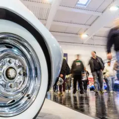 Detailaufnahme eines Oldtimer-Reifens mit Chromfelge auf einer motorsport expo. Besucher bewegen sich im Hintergrund.