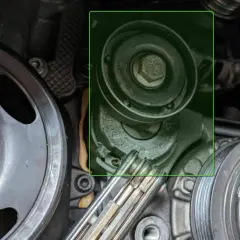 Detailaufnahme eines Keilriemenspanners und Riemenscheiben im Motorraum eines Autos.