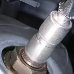 Nahaufnahme einer Lambdasonde, die in ein metallisches Bauteil eingeschraubt ist.