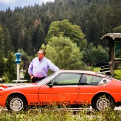 Ein Mann lehnt an seinem leuchtend orangen Simca Matra Bagheera. Im Hintergrund ein dichter Nadelwald.