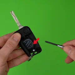 Schlüsselanhänger mit Batterie und Schraubendreher auf grünem Hintergrund.