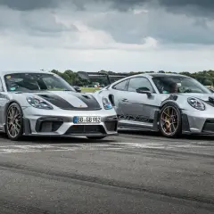 Zwei silberne Porsche GT4 und GT4 RS stehen nebeneinander auf einer Rennstrecke.