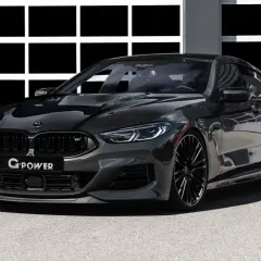 Ein getunter BMW M850 Gran Coupé in dunklem Grau mit Carbon-Elementen und auffälligem Heckspoiler steht vor einer Garage.