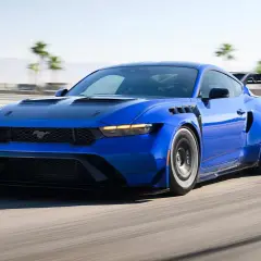 Blauer Mustang GTD rast auf Rennstrecke, mit breiten Kotflügeln und großem Heckspoiler.