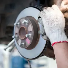 Hände in Handschuhen prüfen eine Bremsscheibe und den Bremssattel eines Autos.