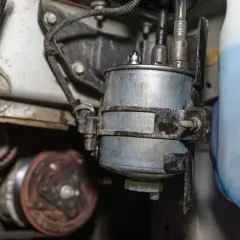 Nahaufnahme eines Kraftstofffilters, der neben einem blauen Behälter montiert ist. Mögliche kraftstoffpumpe defekt symptome könnten hier ihren Ursprung haben.