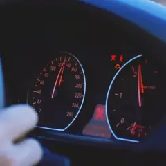 Arm am Lenkrad, Tacho zeigt 120 km/h. Warnleuchten leuchten, mögliche Motorschaden Symptome.