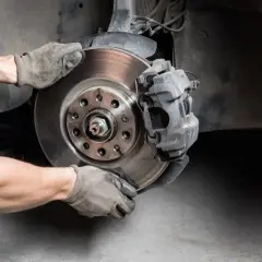 Hände in Handschuhen wechseln Bremsscheibe und Bremssattel an einem Auto.