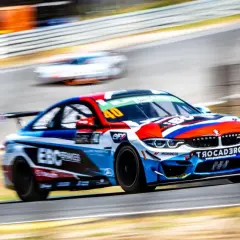 Ein BMW GT4-Rennwagen in voller Fahrt, mit lebendigen Farben und Sponsorenlogos, rast auf einer Rennstrecke.