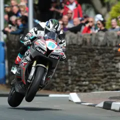 Motorradrennfahrer hebt beim Isle of Man TT ab, Zuschauer im Hintergrund.