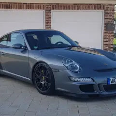 Grauer Porsche 997.1 GT3 mit schwarzem Heckspoiler und Felgen steht vor einer Garage.