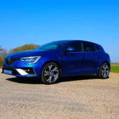 Blauer Renault Mégane 4 RS steht auf einem Feldweg vor grünen Feldern und Bäumen.