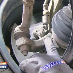 Nahaufnahme eines Audi A4 B6 Fahrwerks mit einem Handschuh, der auf den ABS-Sensor zeigt.
