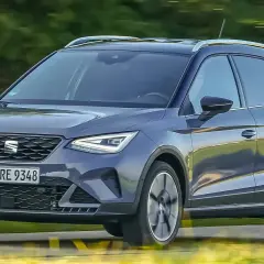 Dunkelgrauer Seat Arona fährt auf einer Straße, Bäume im Hintergrund.