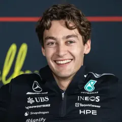 George Russell lächelt breit in seinem Mercedes-Team-Outfit. Sein Gehalt ist ein heiß diskutiertes Thema unter Fans.