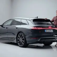 Mann steht neben dunklem Audi S6 Avant e-tron mit leuchtenden Rückleuchten.