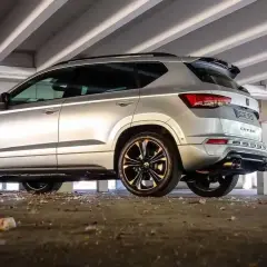 Silberner Cupra Ateca mit Mann, der auf den Auspuff zeigt, unter Betonstreben.