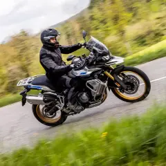 Ein Fahrer auf einer Voge DS 900 X kurvt auf einer Landstraße durch eine grüne Landschaft.