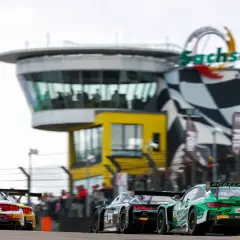 Rennwagen rasen auf dem Sachsenring. Ein grüner BMW mit #GREENMACHINE-Schriftzug und ein roter Ford Mustang liefern sich ein spannendes DTM-Rennen.